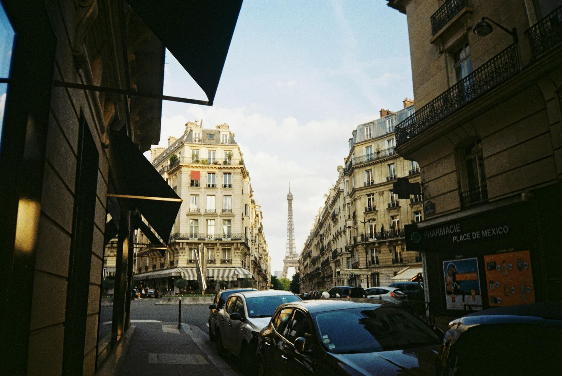 A classic Paris cityscape featuring the Eiffel Tower framed by elegant Haussmann buildings in a busy street.