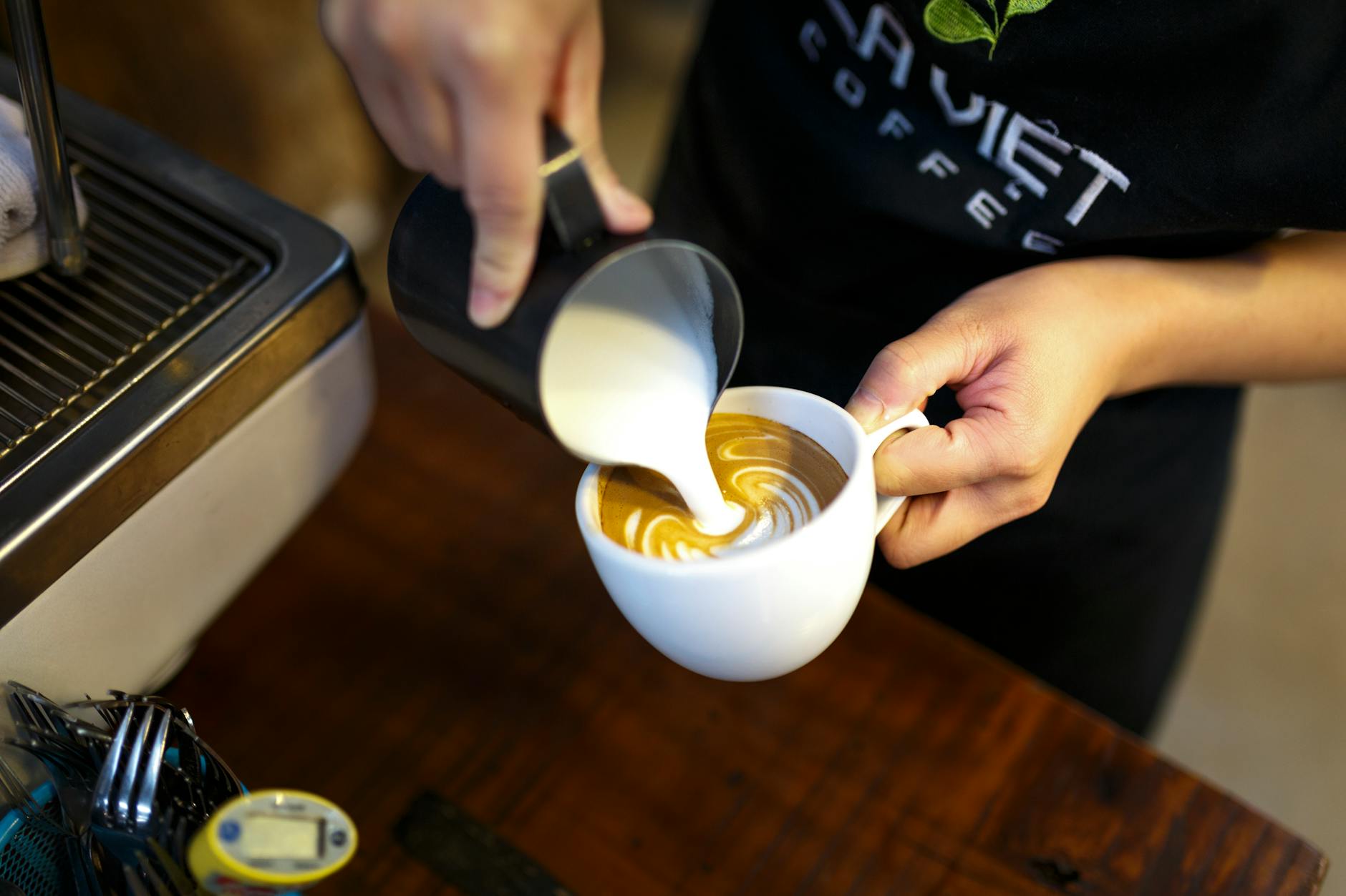 A barista expertly pours milk to create beautiful latte art in a cozy coffee shop setting.