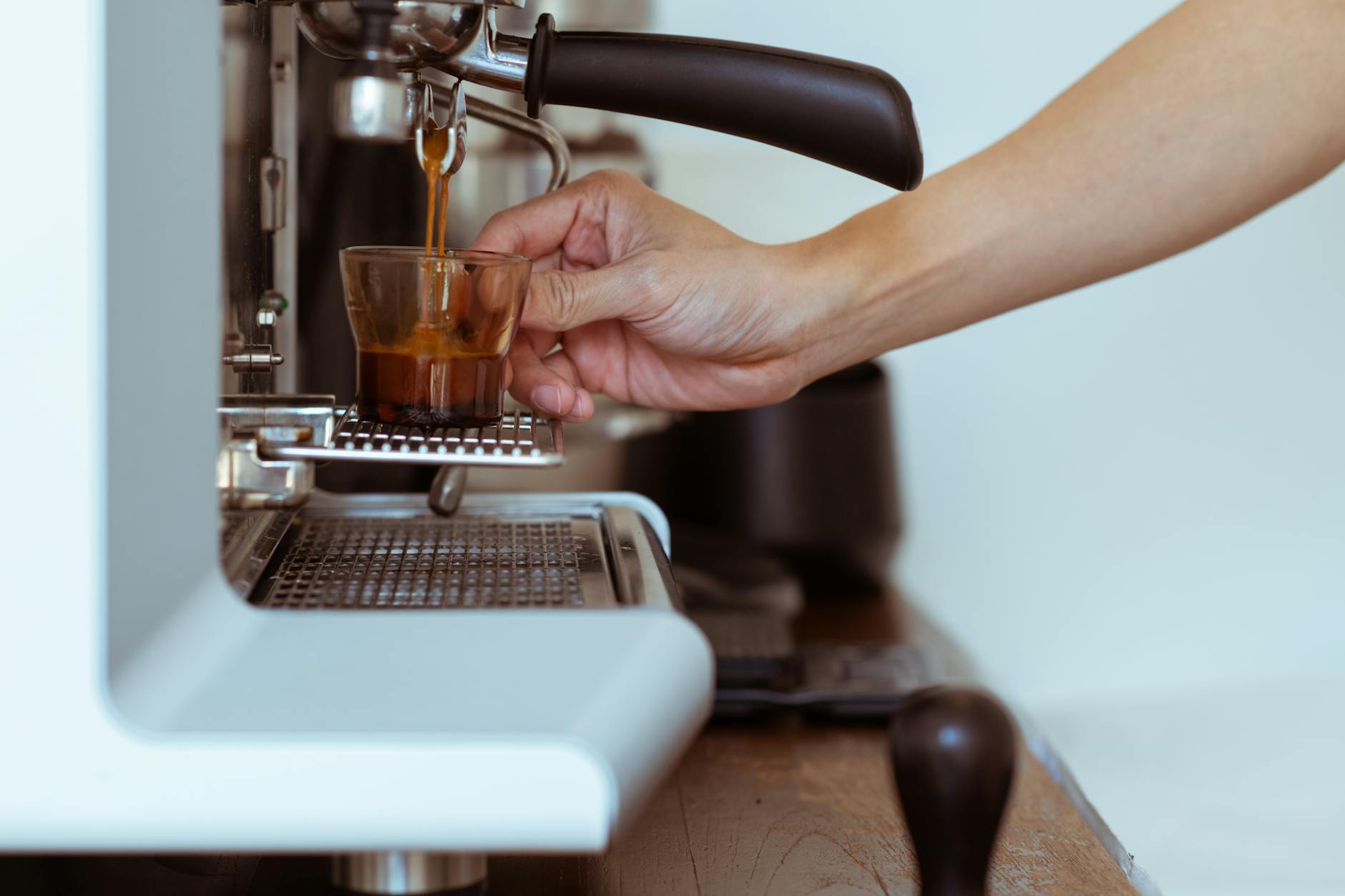 Close-up of a barista's hand pouring espresso from a machine into a glass cup.
