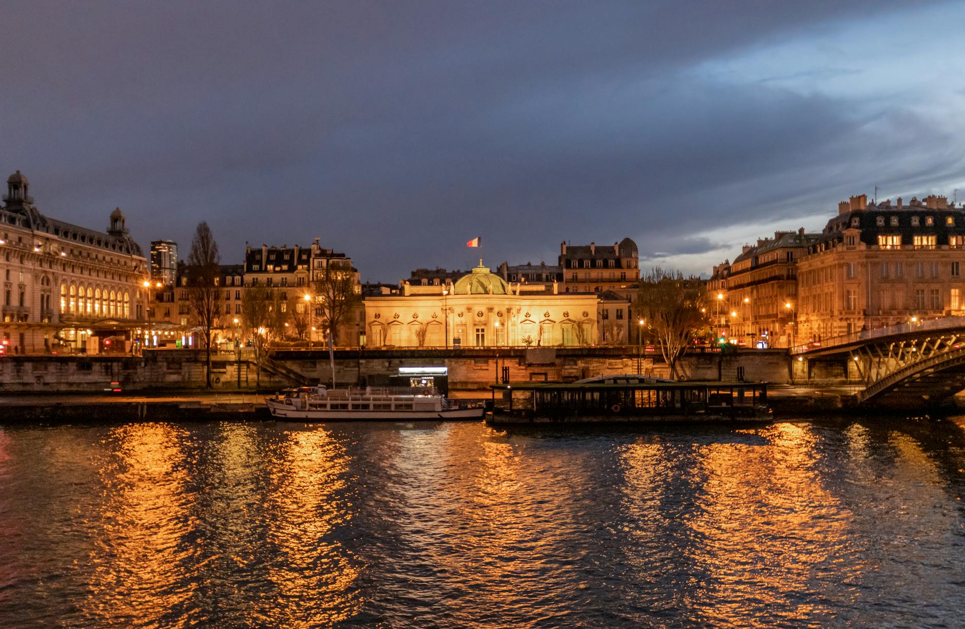 Illuminated Parisian landmarks and bridges reflecting in the Seine at night.