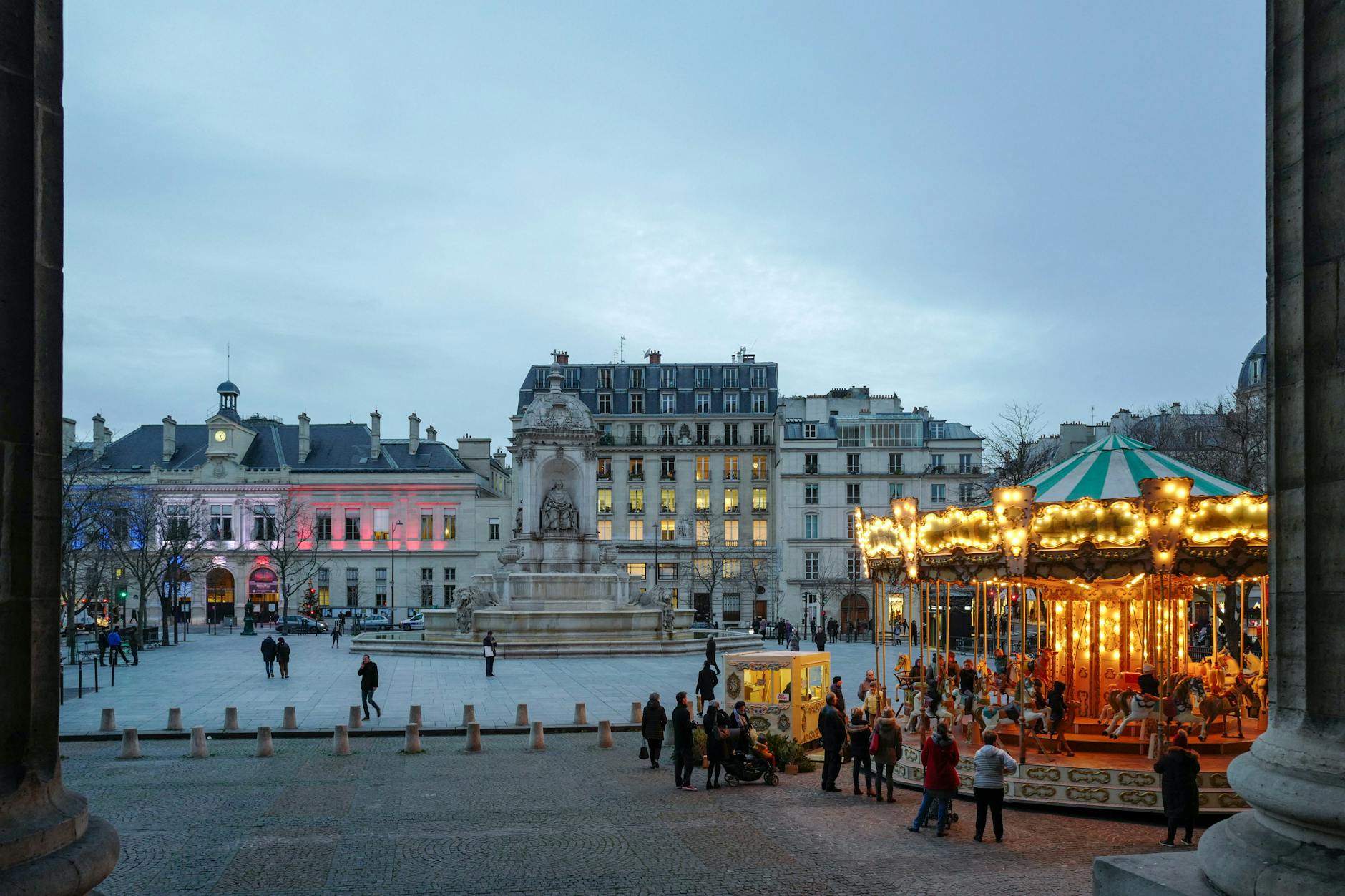 Vibrant carousel lights up a Parisian square at dusk, offering a charming urban scene.