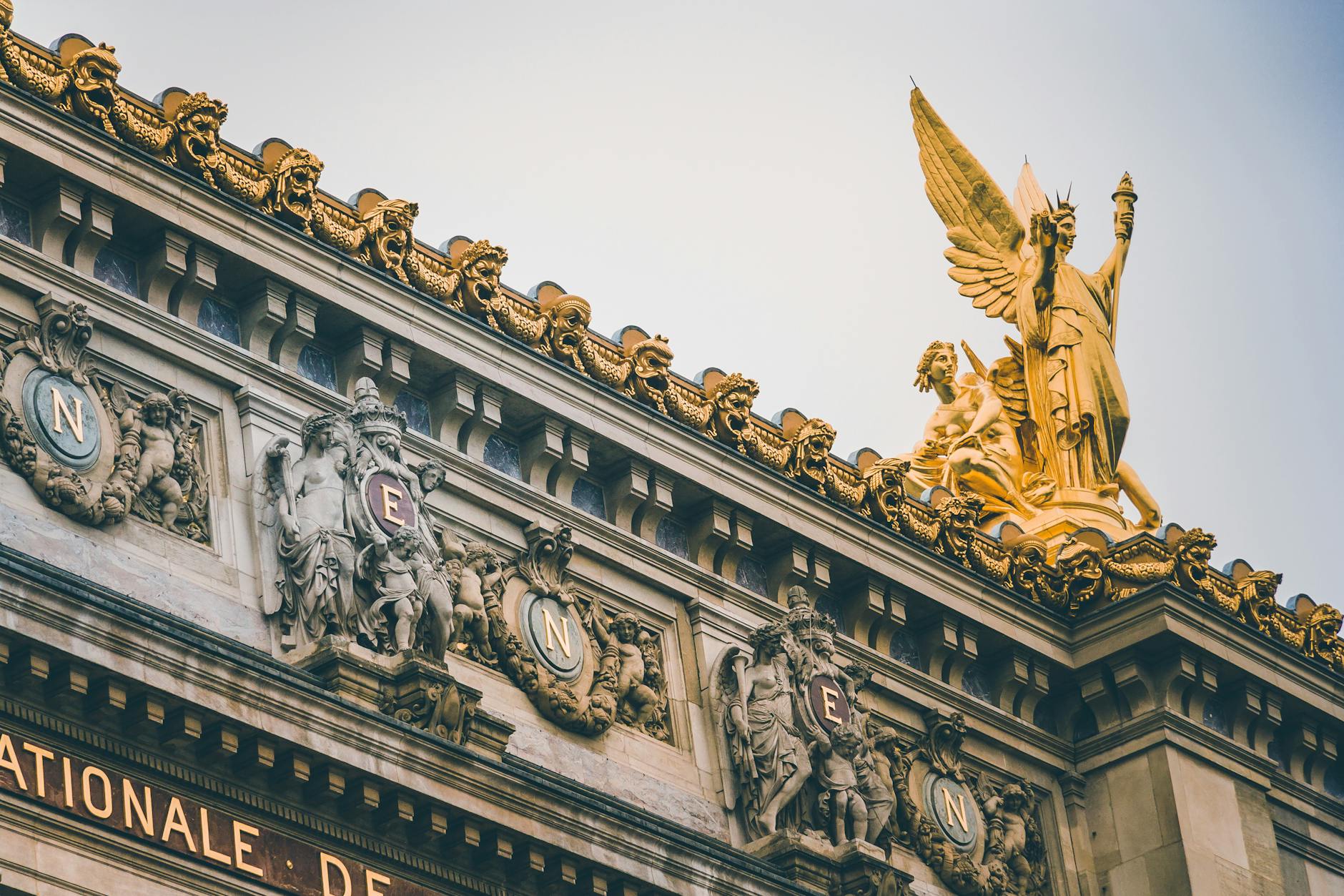 Low angle view of ornate sculptures and golden statues at Palais Garnier, Paris.