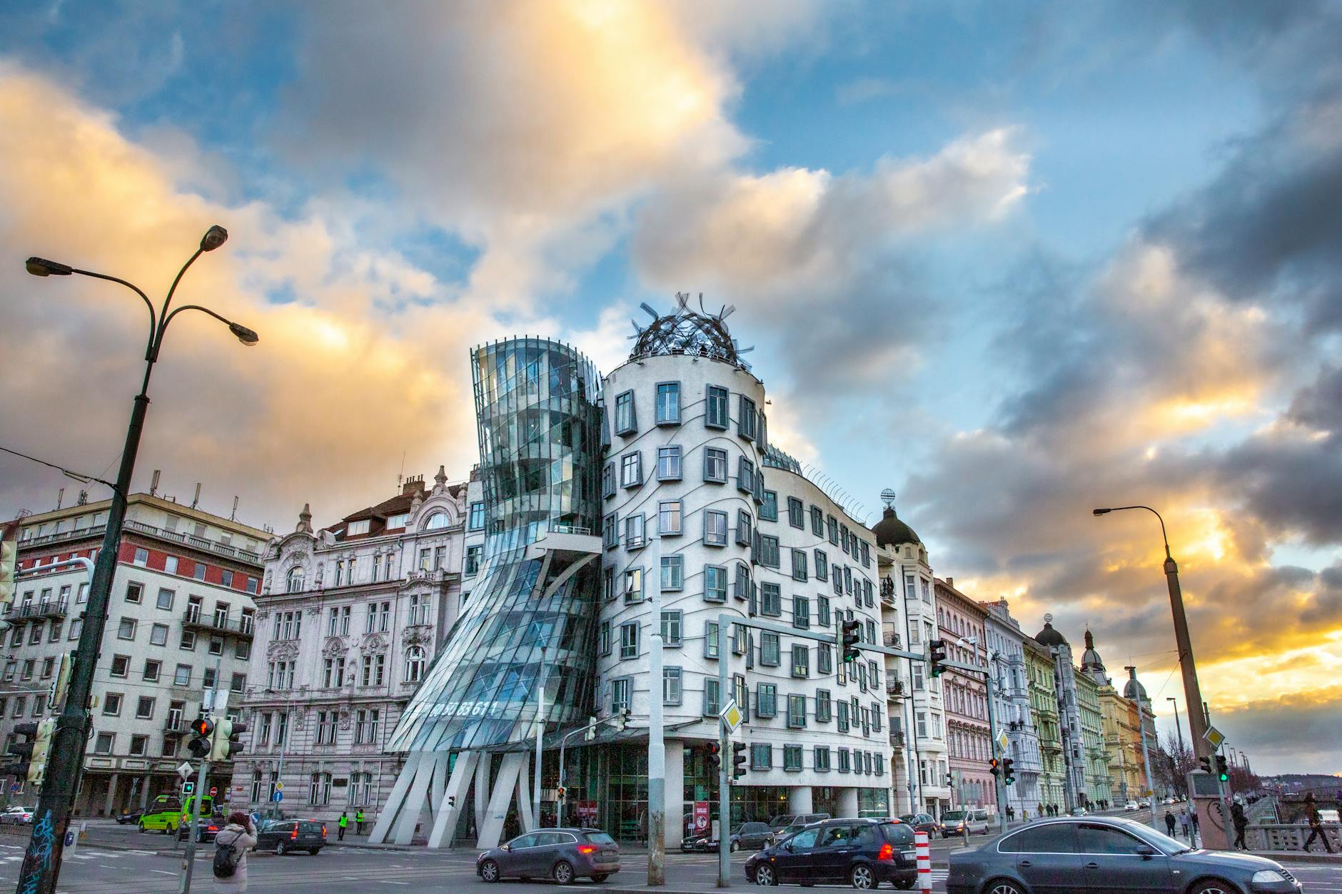 The Dancing House in Prague captured at sunset with a dramatic sky and street activity.