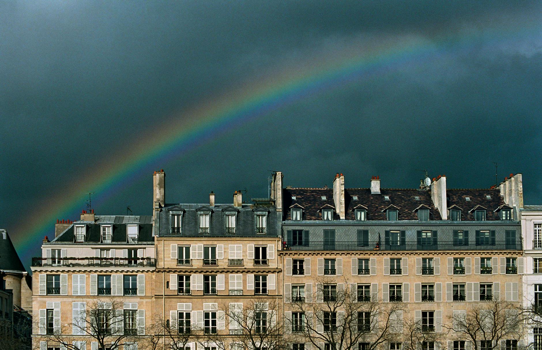 Parisian buildings with a beautiful rainbow arched overhead against a dramatic sky, capturing the city's charm.