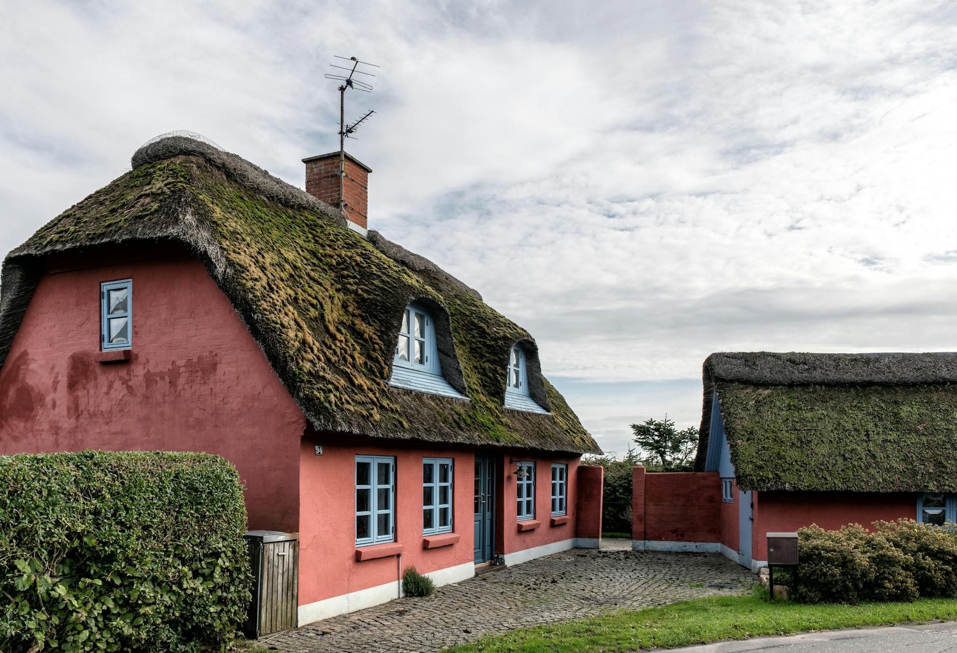 Charming thatched cottages with red walls in Haderslev, Denmark under a cloudy sky.