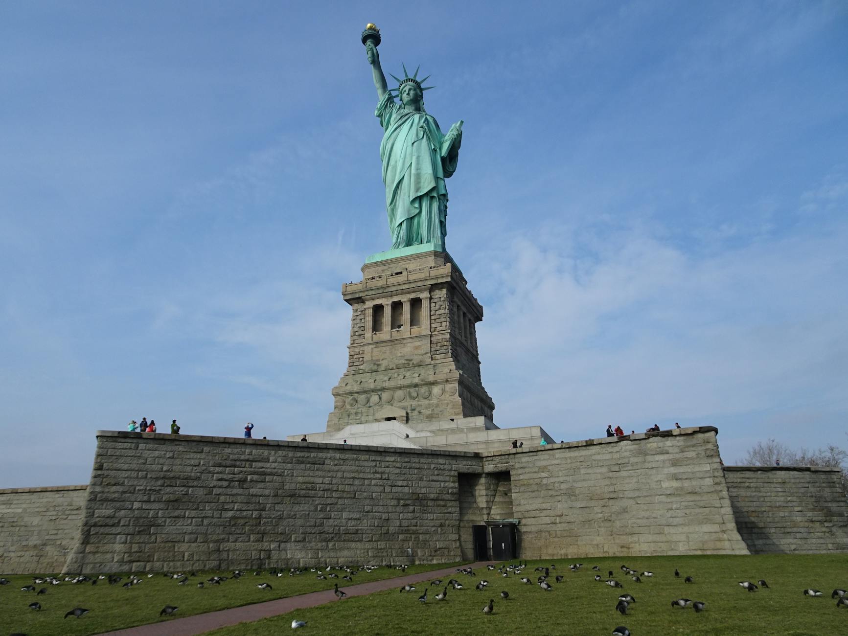 The Statue of Liberty stands tall against a blue sky in New York City, surrounded by birds.