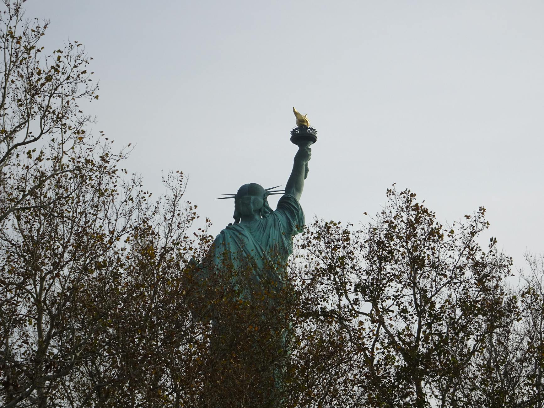 Back view of the Statue of Liberty with autumn trees, highlighting the iconic torch.