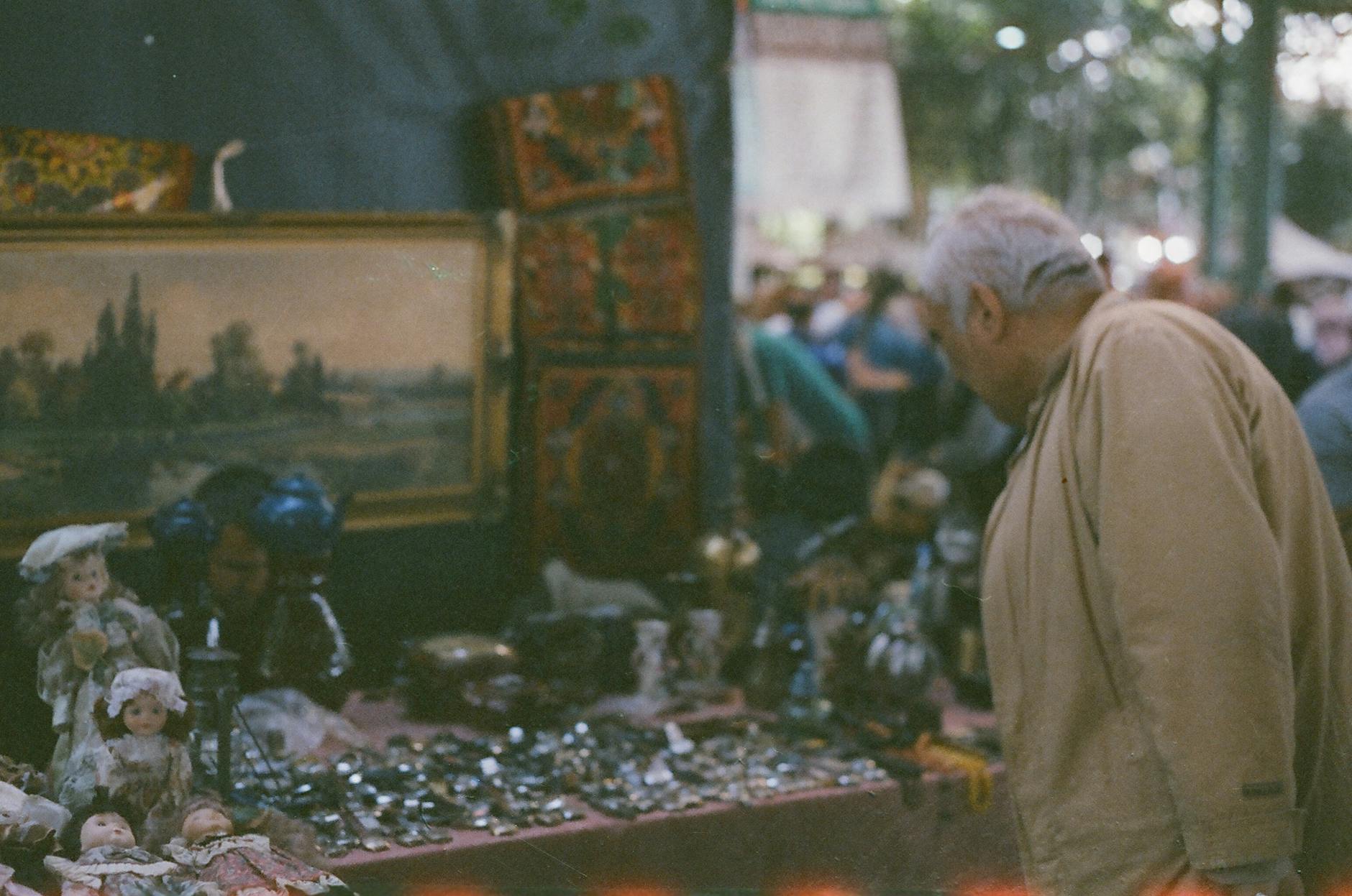 Elderly man examining collectibles at an outdoor antique market display.