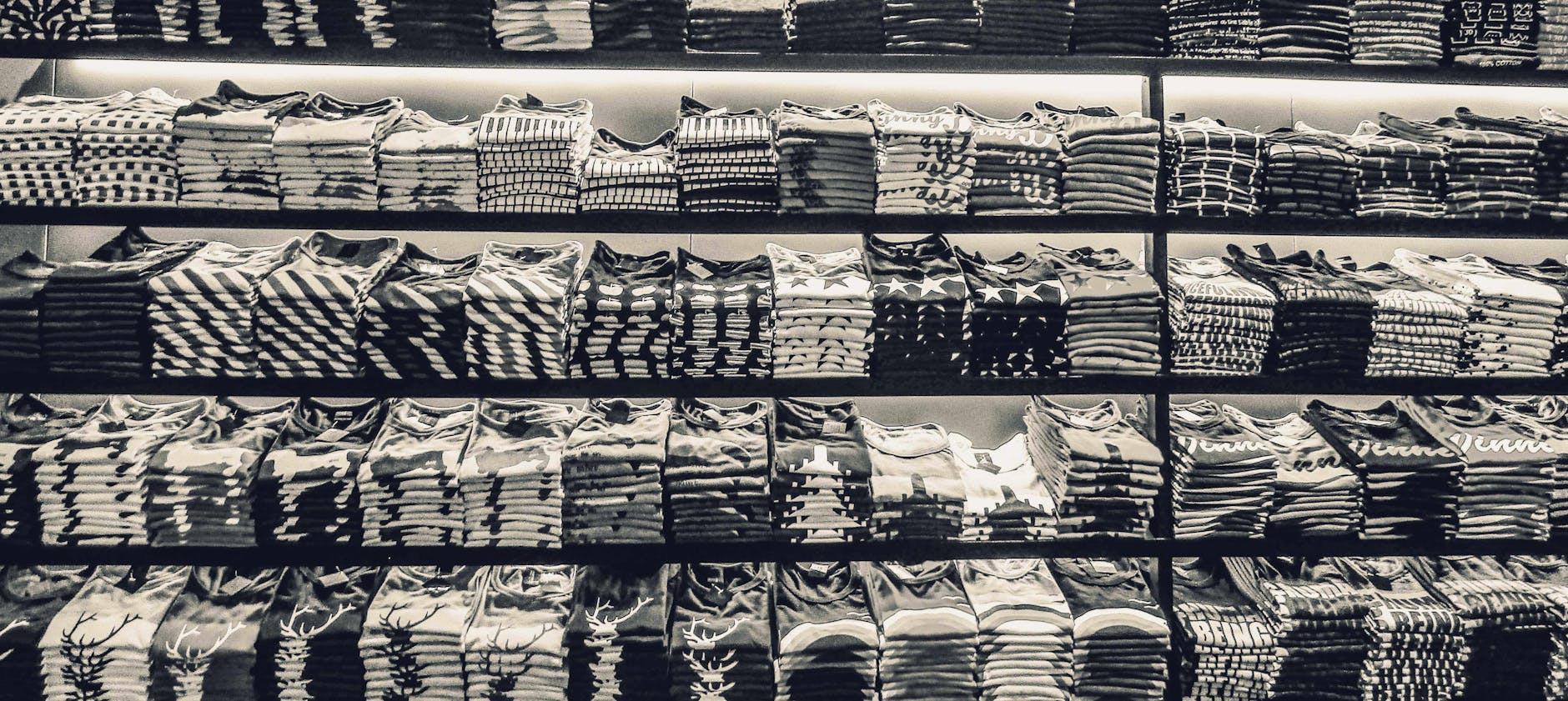 Black and white image showcasing neatly folded t-shirts stacked on store shelves.