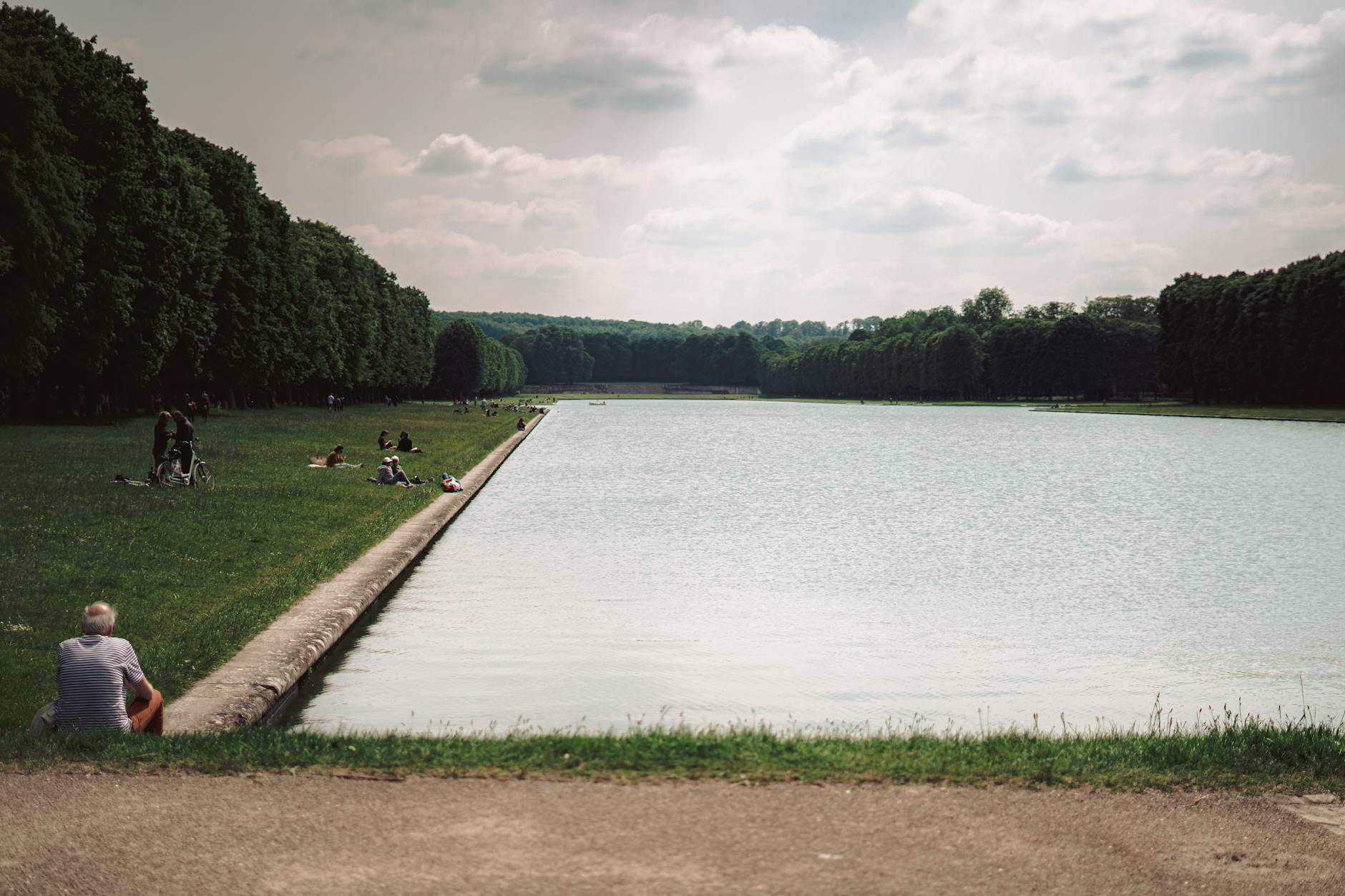 People enjoying a sunny day by the canal in the gardens of Versailles.