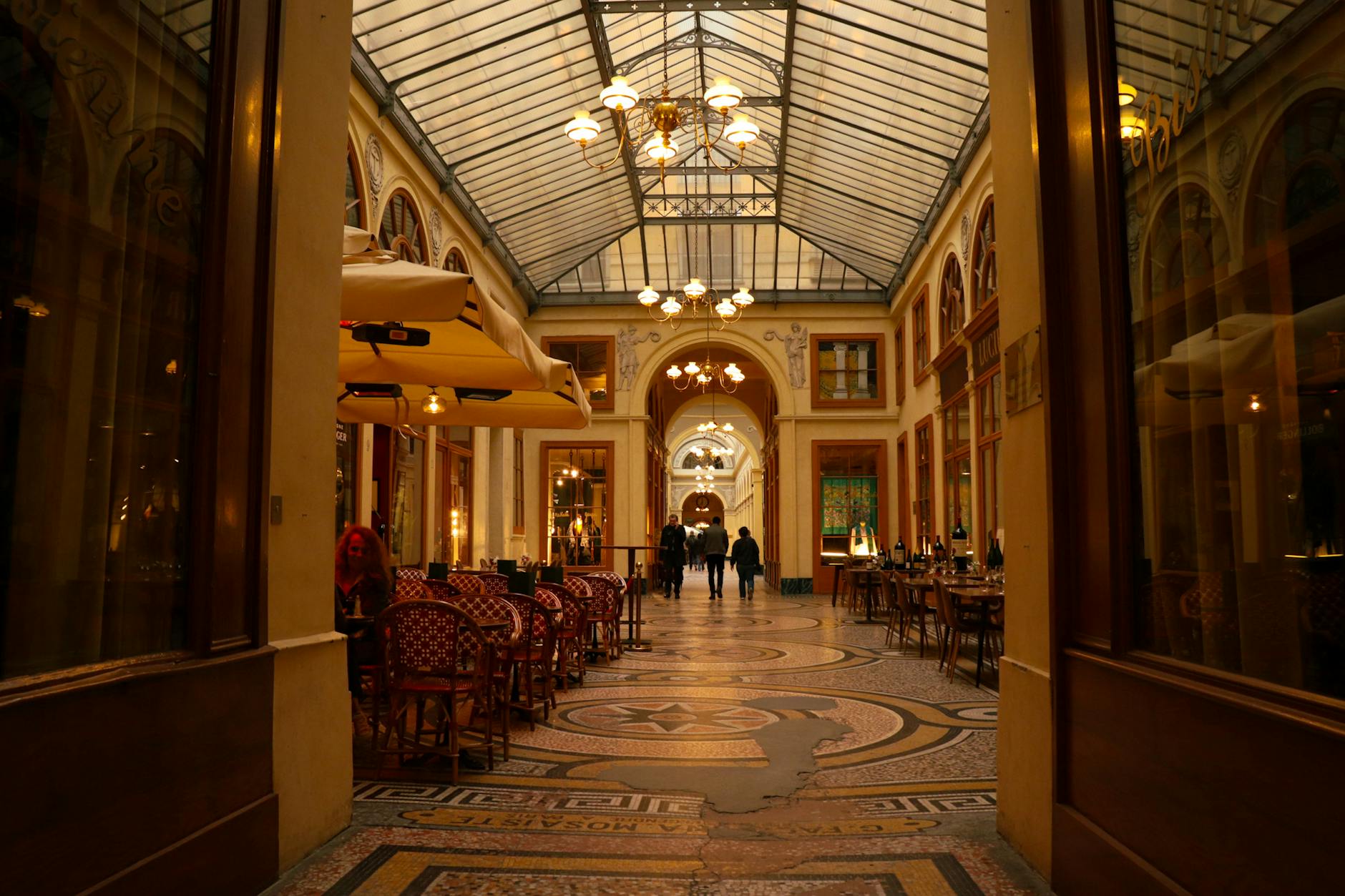 Charming indoor passageway with arches, ambient lighting, and café seating, showcasing elegant architecture.