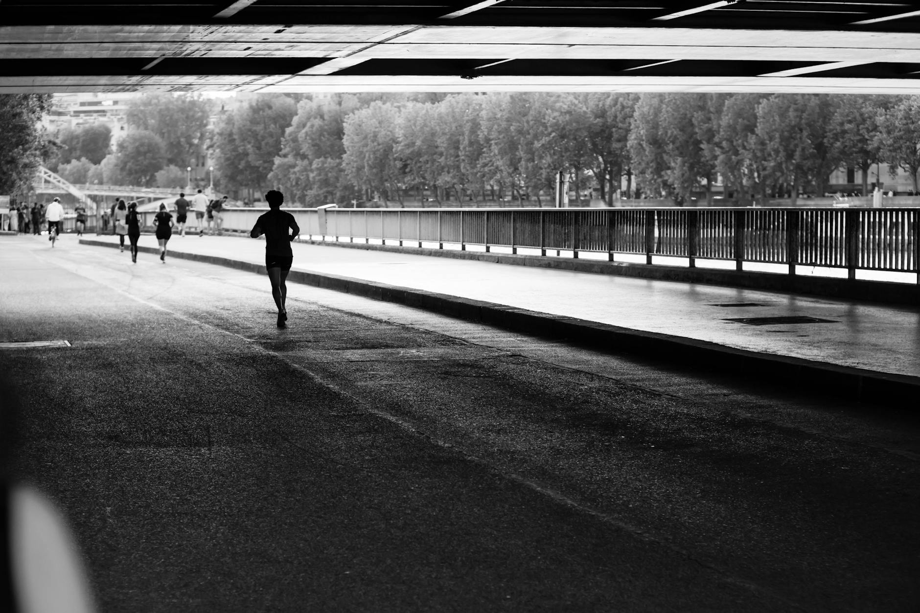 Black and white photo of people jogging along the Seine River in Paris, capturing urban fitness lifestyle.