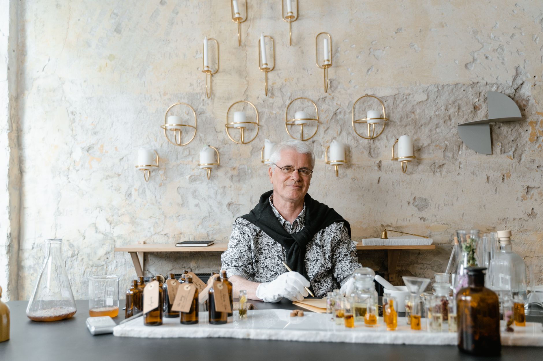Senior male perfumer sitting among fragrance bottles in a rustic setting, creating unique scents.