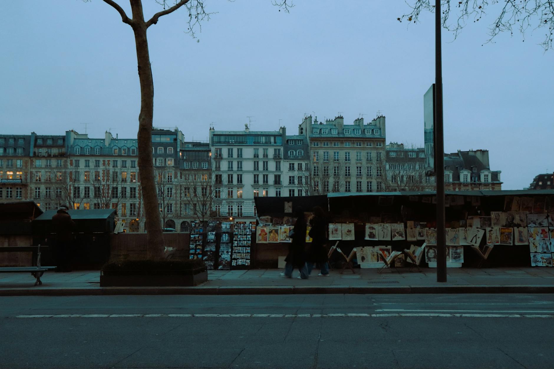 Explore the enchanting art stalls along a Paris street at dusk, showcasing vibrant prints.