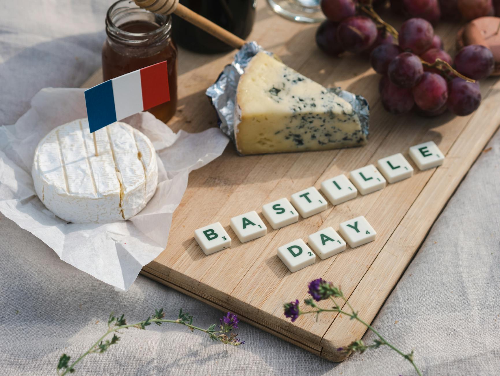 Celebrate Bastille Day with a festive picnic featuring French cheese, grapes, and scrabble tiles.