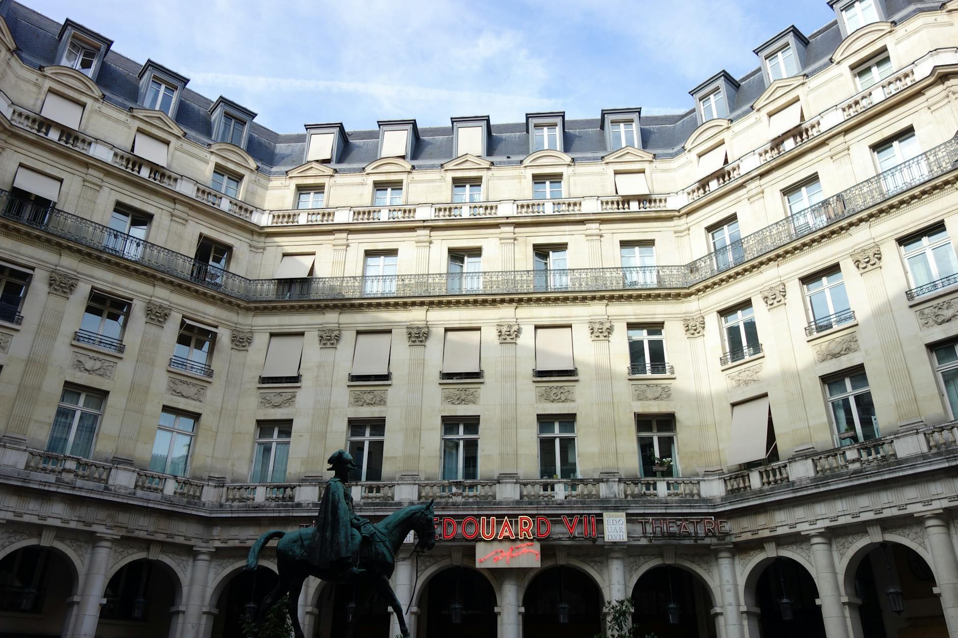 Elegant architecture of Edouard VII Theatre courtyard in Paris with a statue at the center.