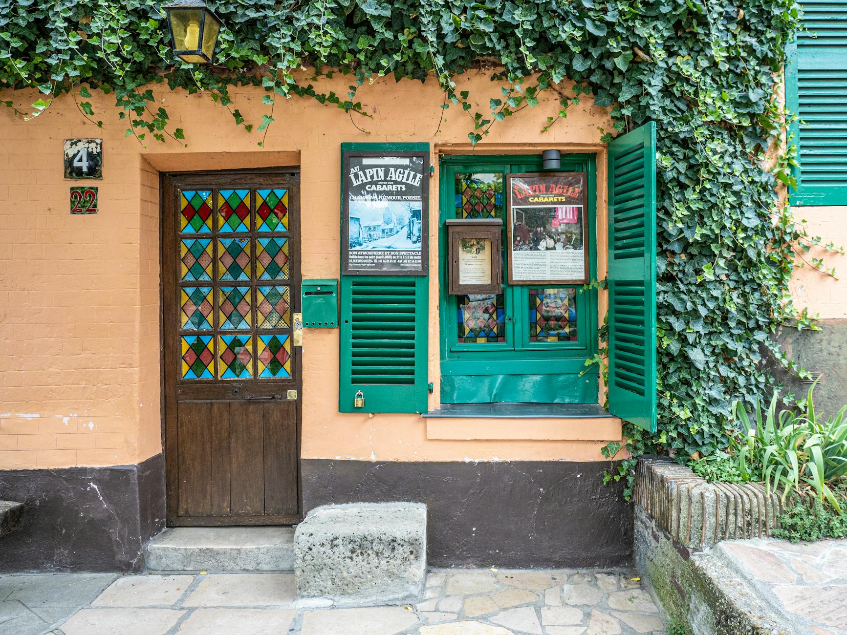 Vibrant facade of Lapin Agile cabaret in Montmartre, Paris, covered with ivy and colorful door.