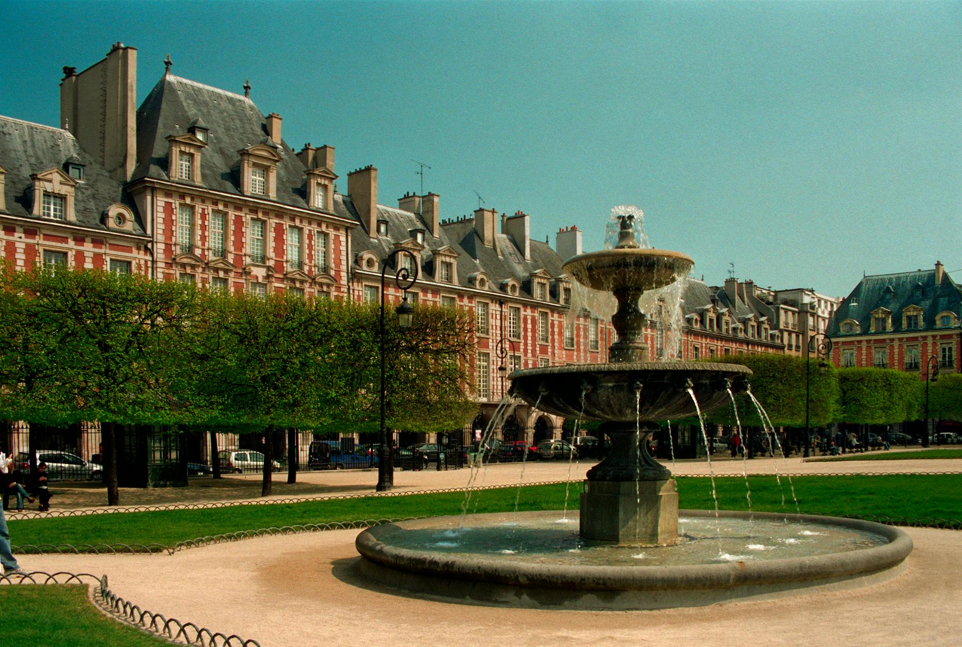 View of the iconic Place des Vosges with fountain in Paris, France, under a clear sky.