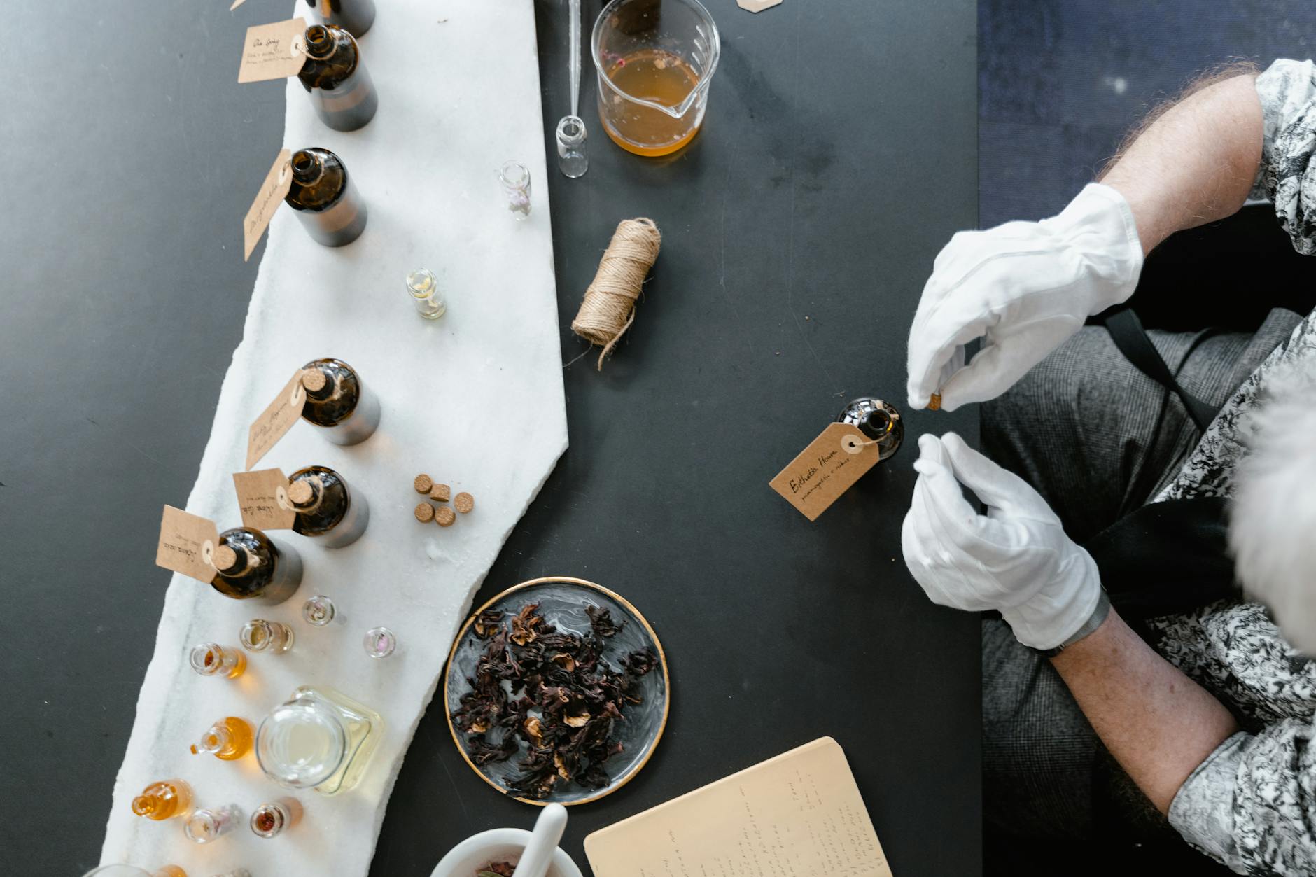 Overhead view of a perfume-making workshop featuring gloves, glass bottles, and natural ingredients.