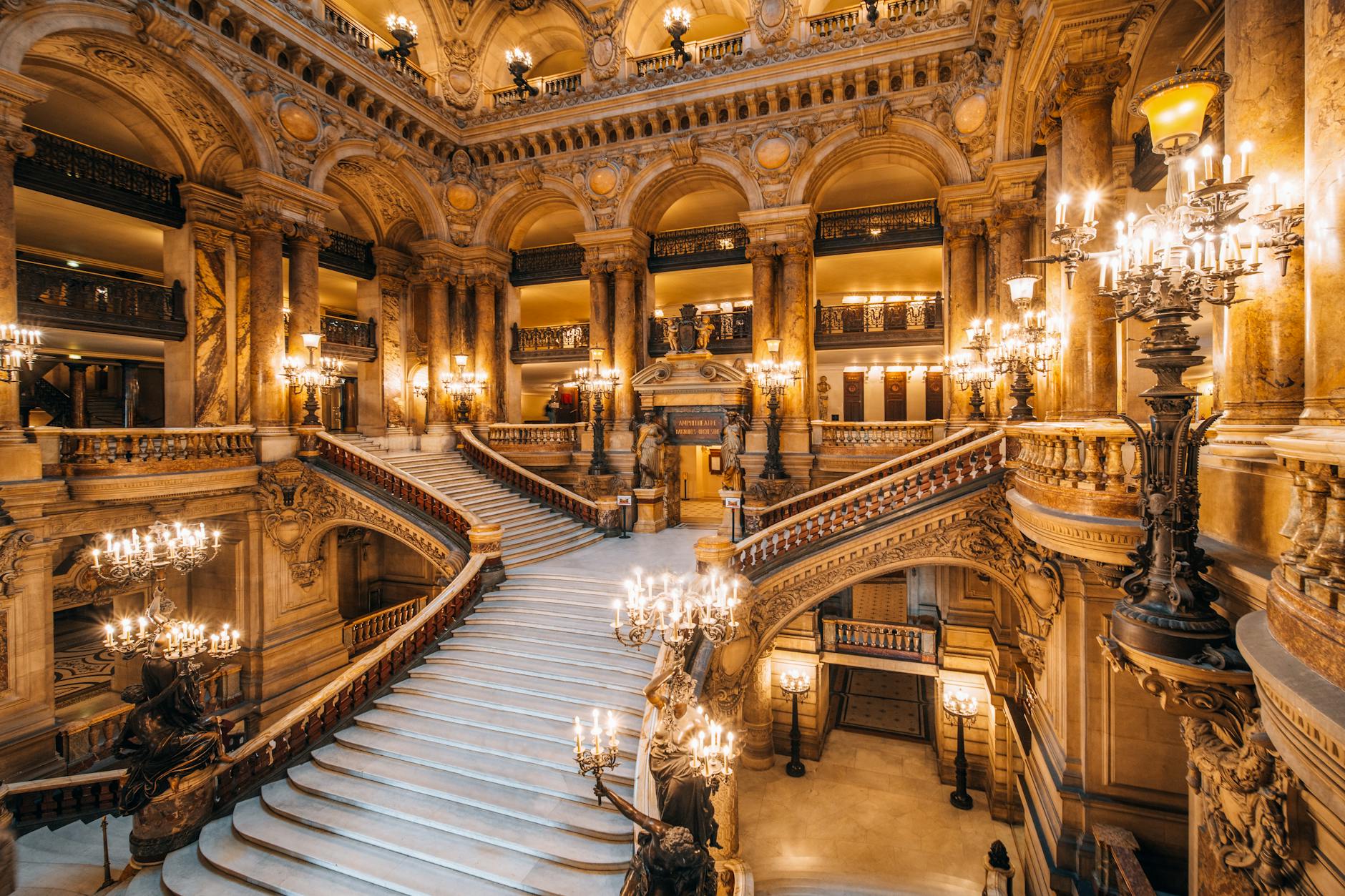 Stunning view of a grand ornate opera house staircase illuminated with chandeliers.