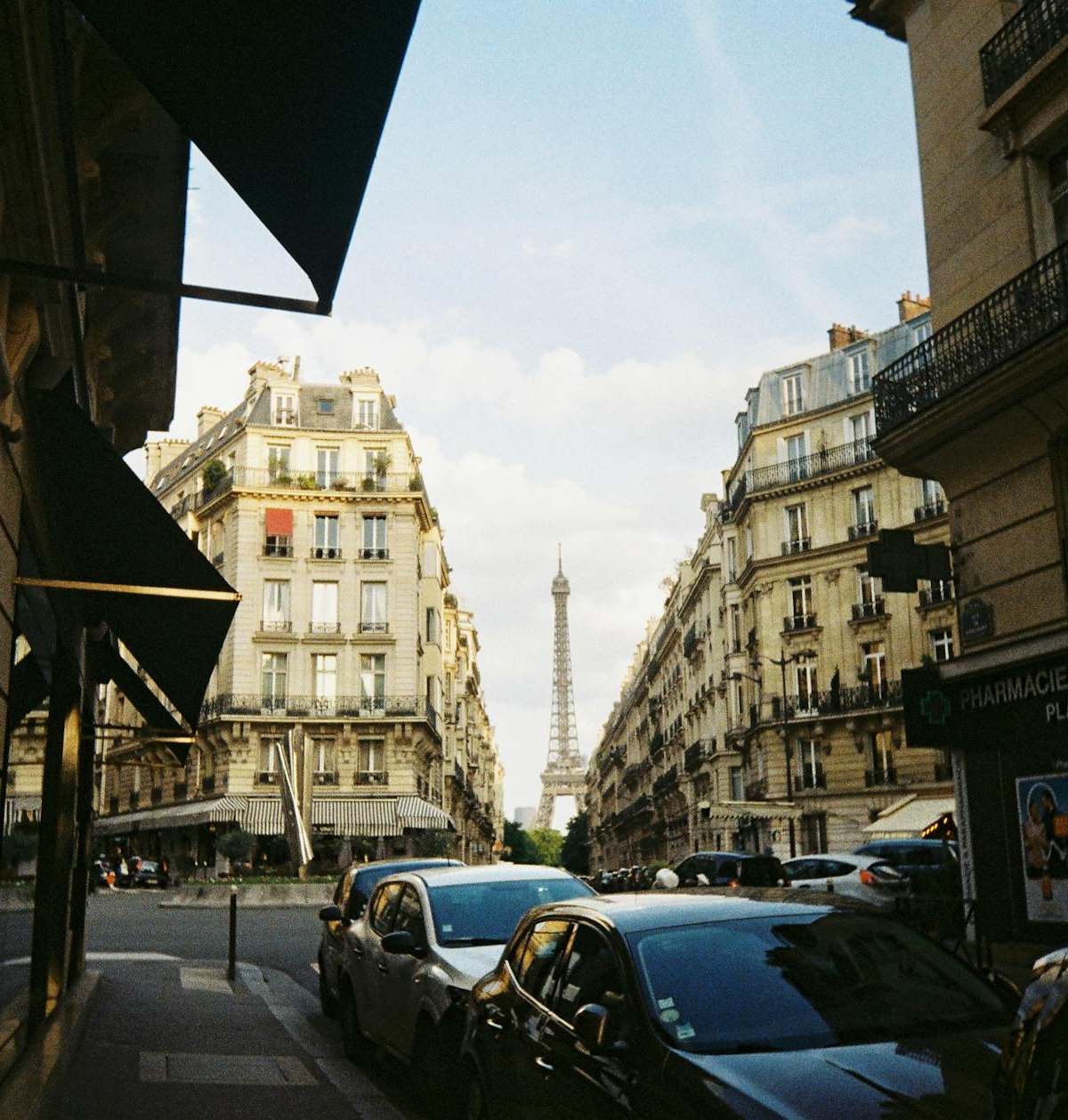 A classic Paris cityscape featuring the Eiffel Tower framed by elegant Haussmann buildings in a busy street.