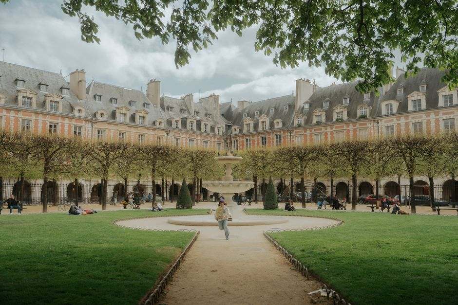Scenic view of Place des Vosges in Paris with people enjoying leisure time under lush greenery.