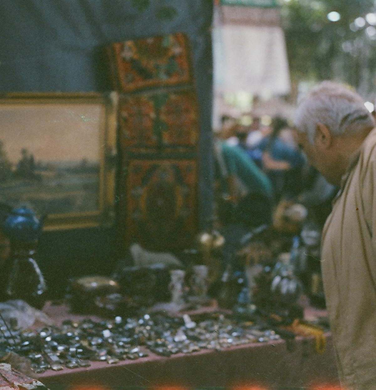 Elderly man examining collectibles at an outdoor antique market display.