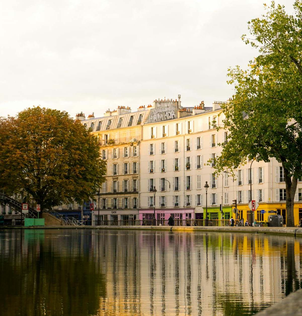 Scenic view of Canal Saint-Martin in Paris with footbridge and colorful buildings reflecting in the water.