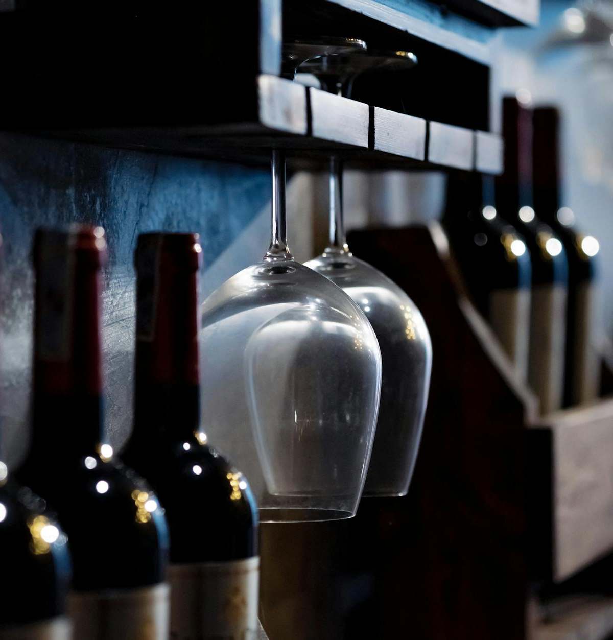 Close-up of wine bottles and glasses on wooden shelves in a dimly lit cellar, creating a cozy ambiance.