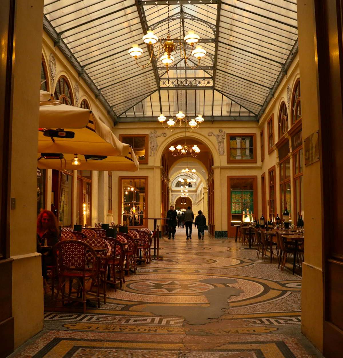 Charming indoor passageway with arches, ambient lighting, and café seating, showcasing elegant architecture.