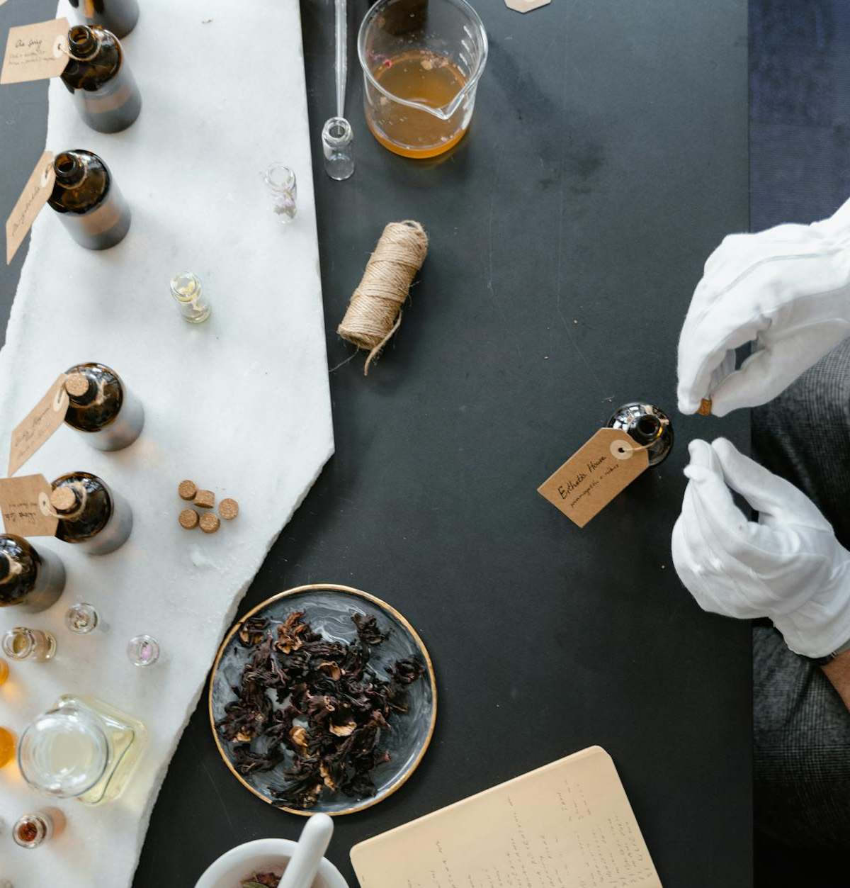 Overhead view of a perfume-making workshop featuring gloves, glass bottles, and natural ingredients.