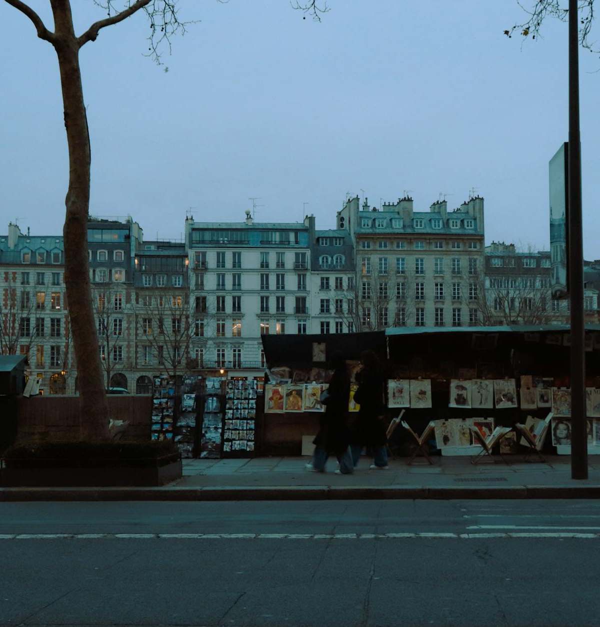 Explore the enchanting art stalls along a Paris street at dusk, showcasing vibrant prints.
