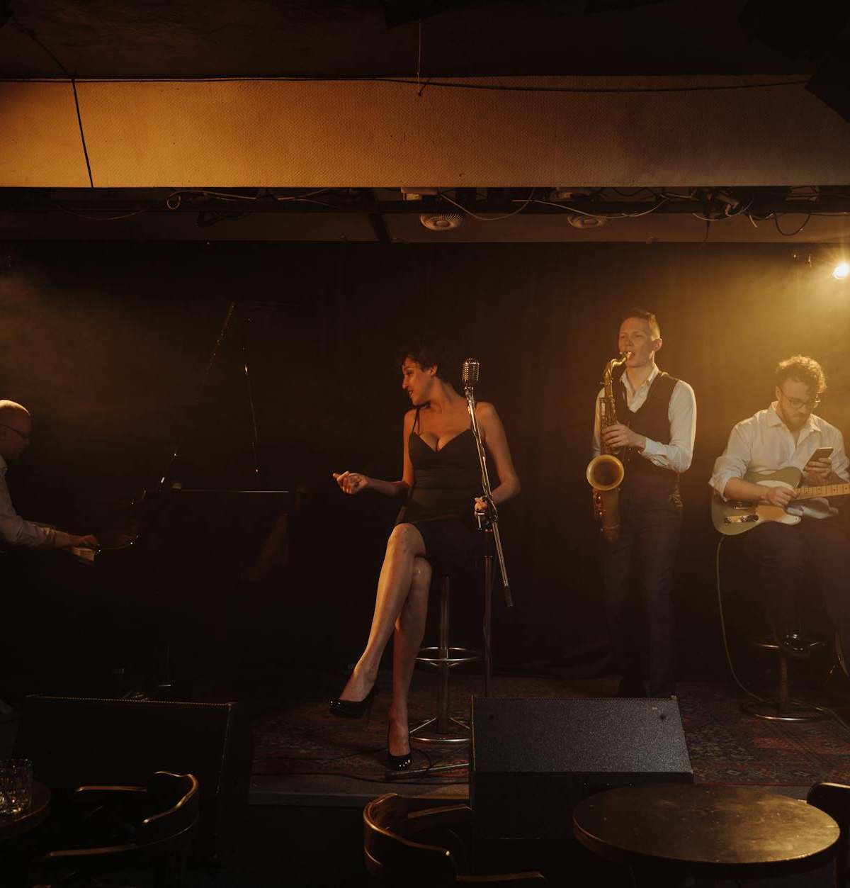 A jazz band performing with a female singer and musicians playing piano, saxophone, and guitar on stage.