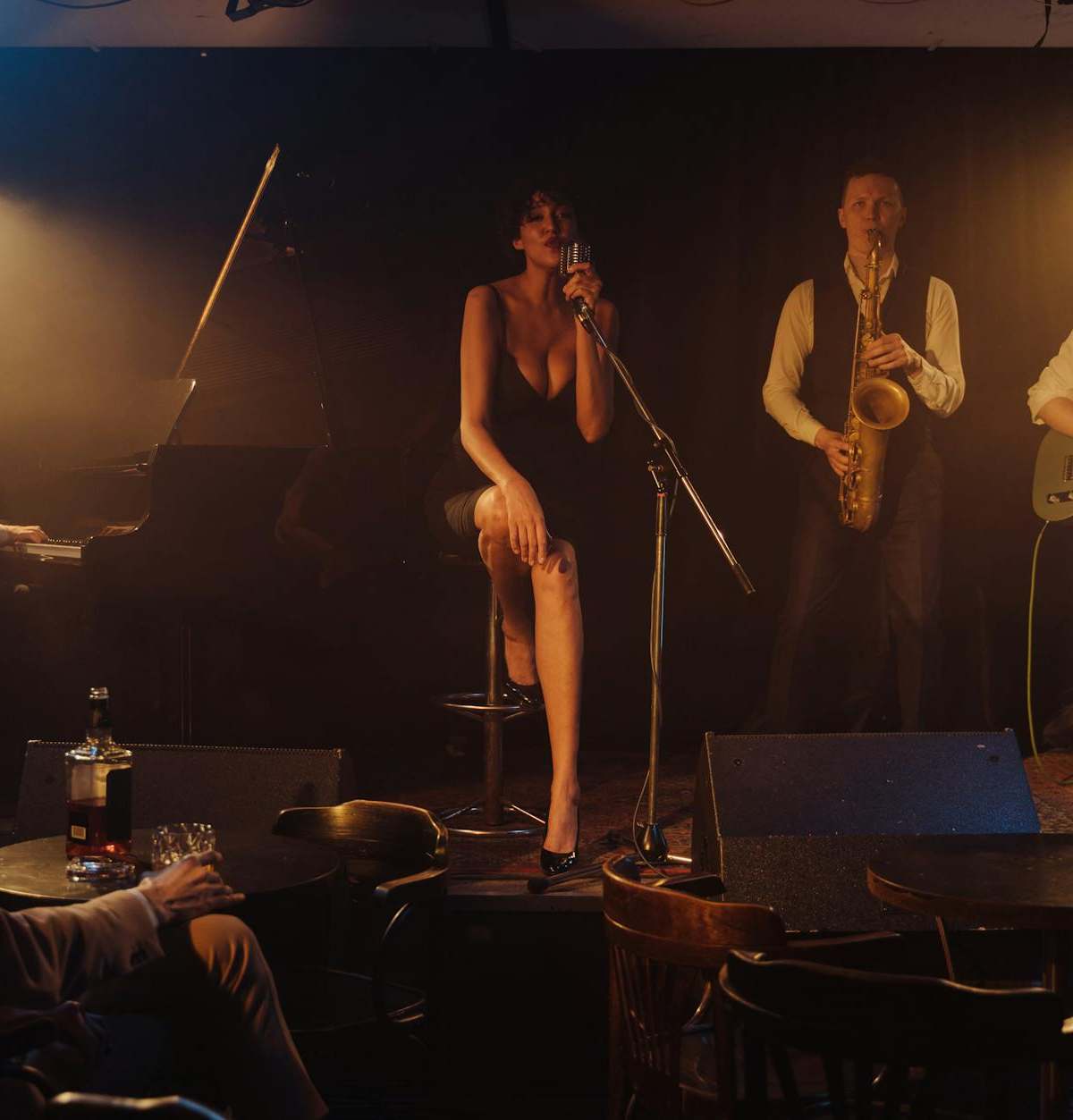 A jazz band performs live on stage in a dimly lit club with a singer and musicians playing various instruments.